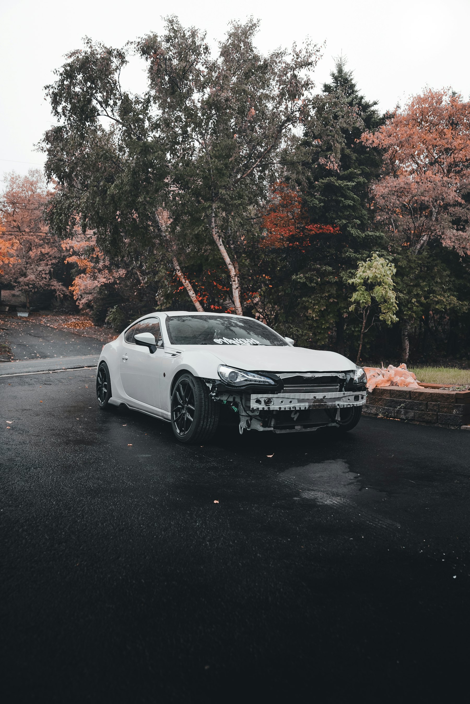 White car with a damaged front bumper on a wet road
